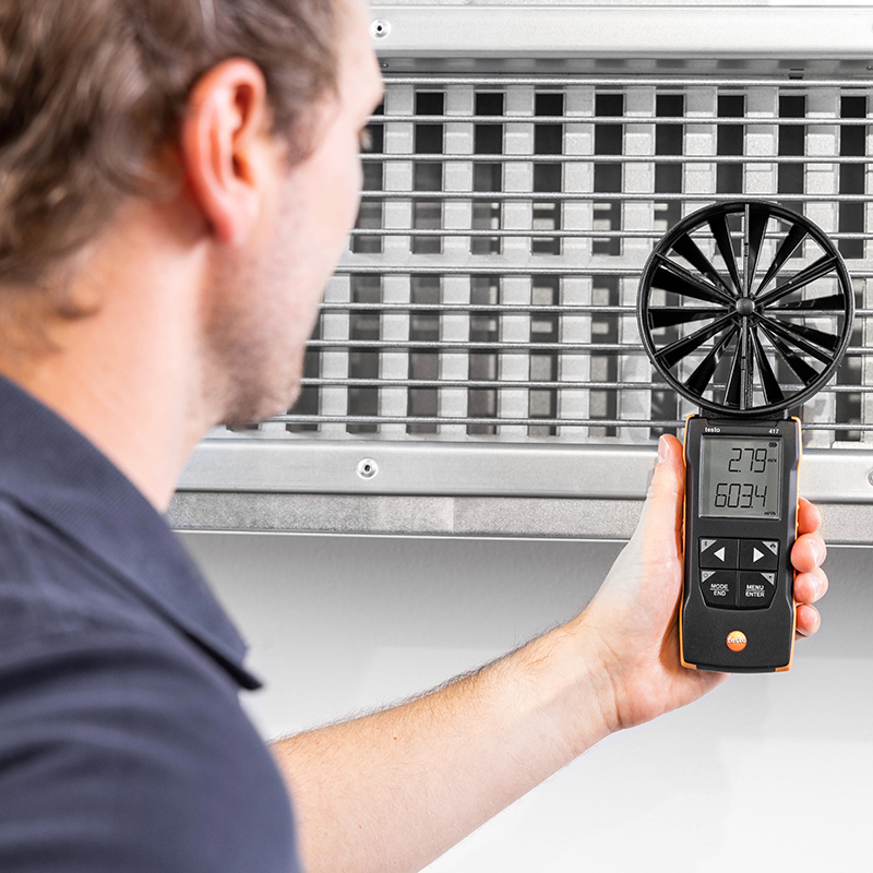 A man in a blue polo t-shirt holds the Testo 417 Vane Anemometer against an air conditioning outlet. 