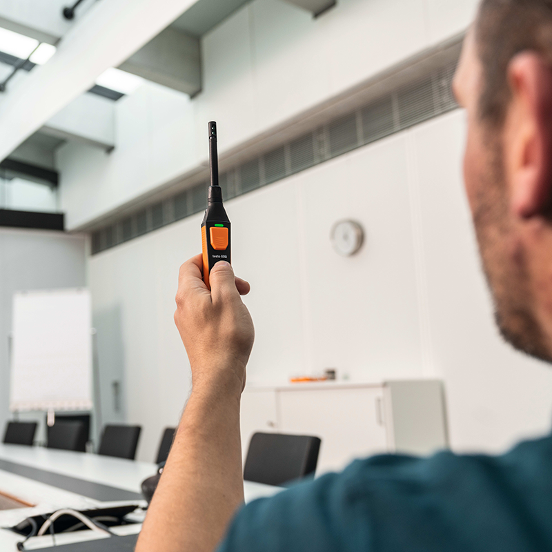 A man holds the Testo 605i Thermohygrometer up in an office meeting room.