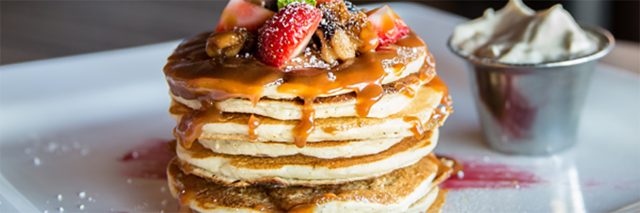 A stack of buttermilk pancakes topped with strawberries and syrup. 