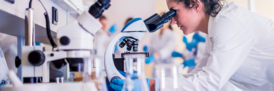 A woman is looking through a microscope in a scientific laboratory. 