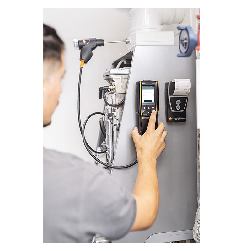 A man uses the Testo 310 Advanced Kit to check a boiler. Both the 310 and Bluetooth printer are magnetically mounted to the side of the boiler; a report is printing from the printer. 